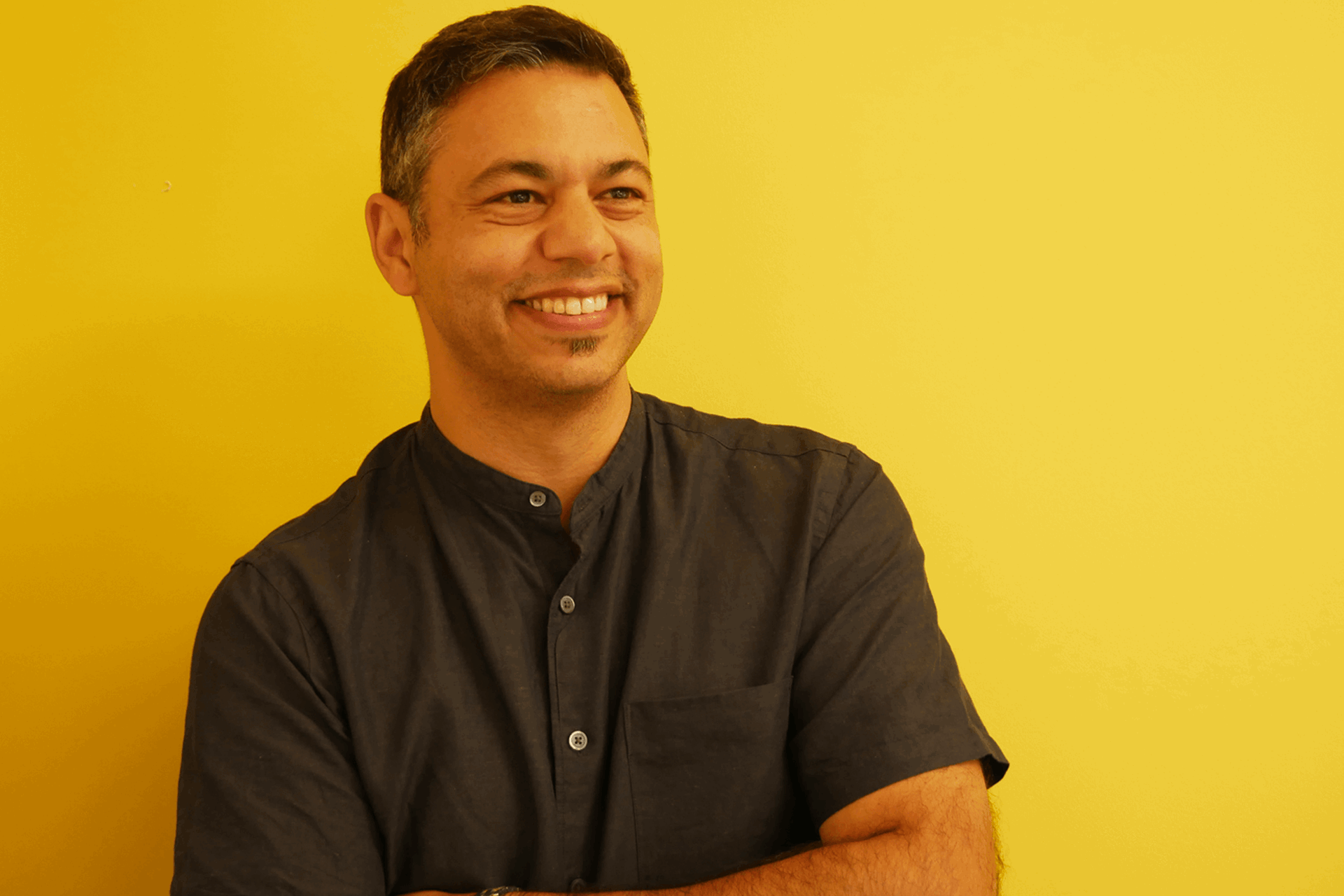 YoungMinds staff member Sacha Dingomal smiling against a yellow background