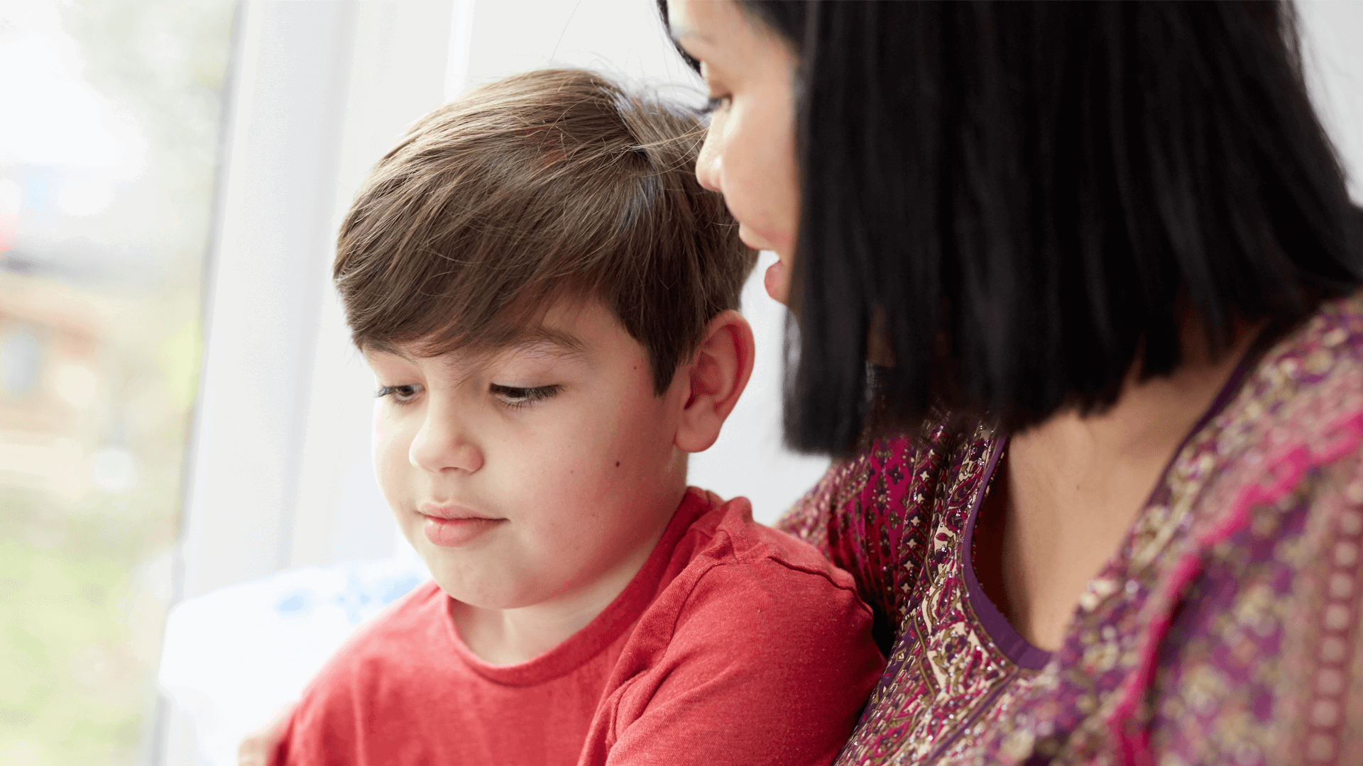 A mother looking at her young son by a window 