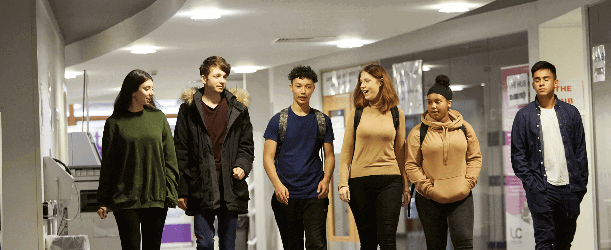 wide shot of six students walking and talking while walking in the hallway of the campus