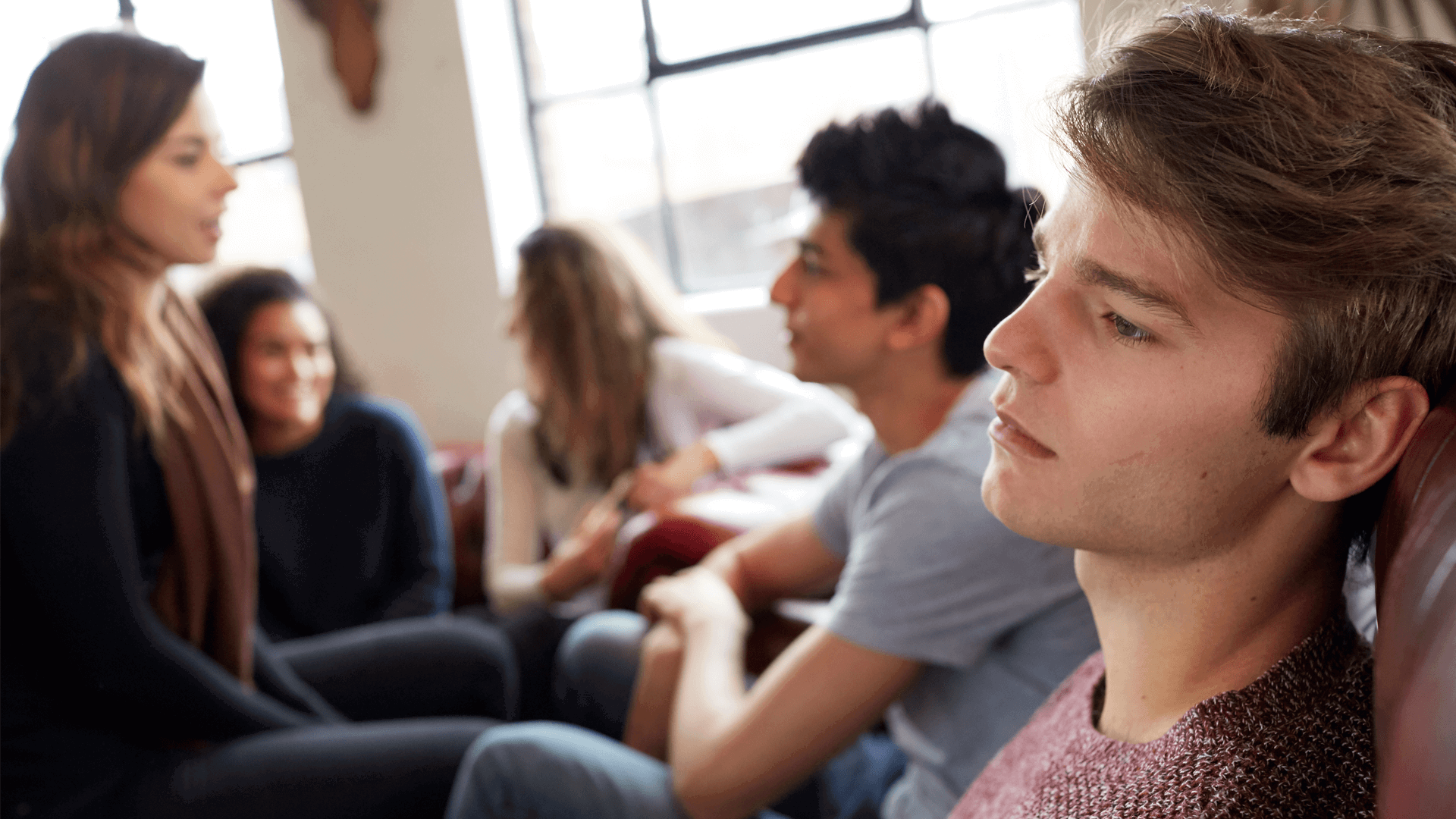 A young person lost in thought while sitting with their group of friends who are talking together.