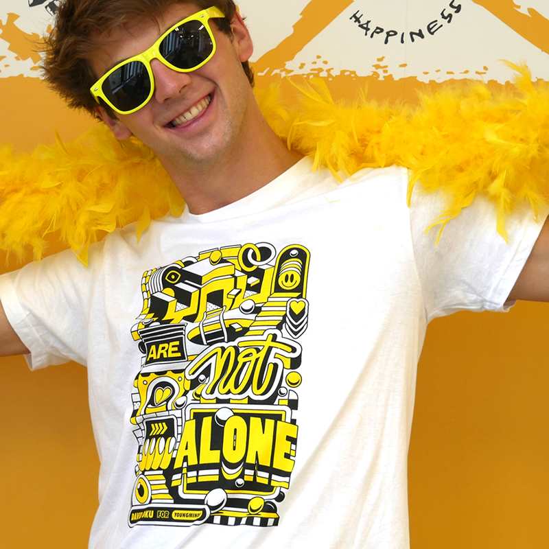 A close up of a man smiling wearing a yellow feather bower, yellow sunglasses and our David Oku's bespoke 'You are not alone' graphic #HelloYellow T-shirt.