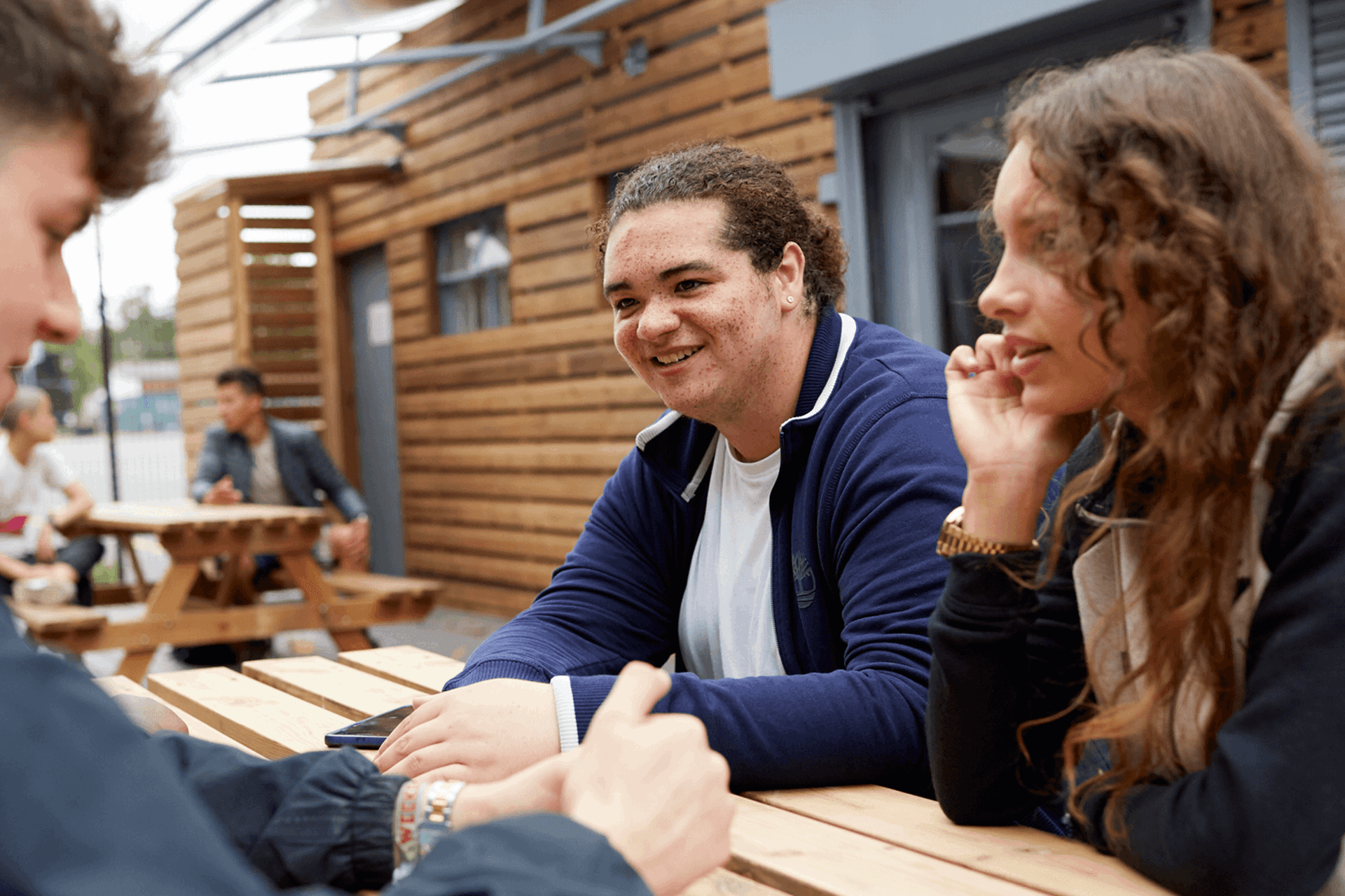 Three young people chatting and smiling while sitting at a picnic bench.