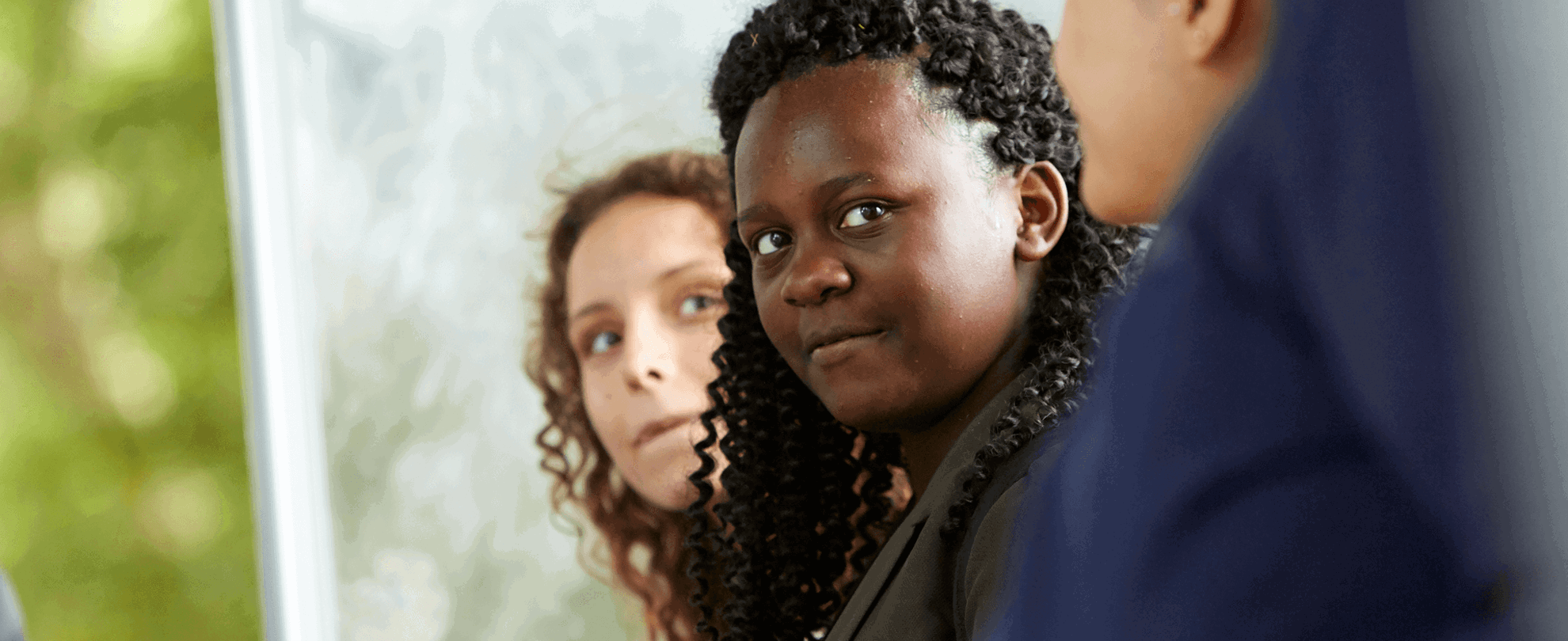 Three young people sitting in a row and talking together in a park.
