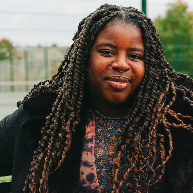 A young Black woman sitting on a bench in the park. She is smiling.