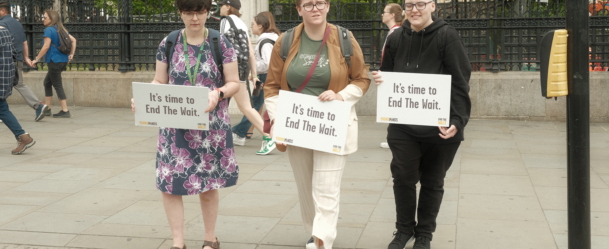 Three Activists holding signs in Parliament Square that read: "It's time to End The Wait."