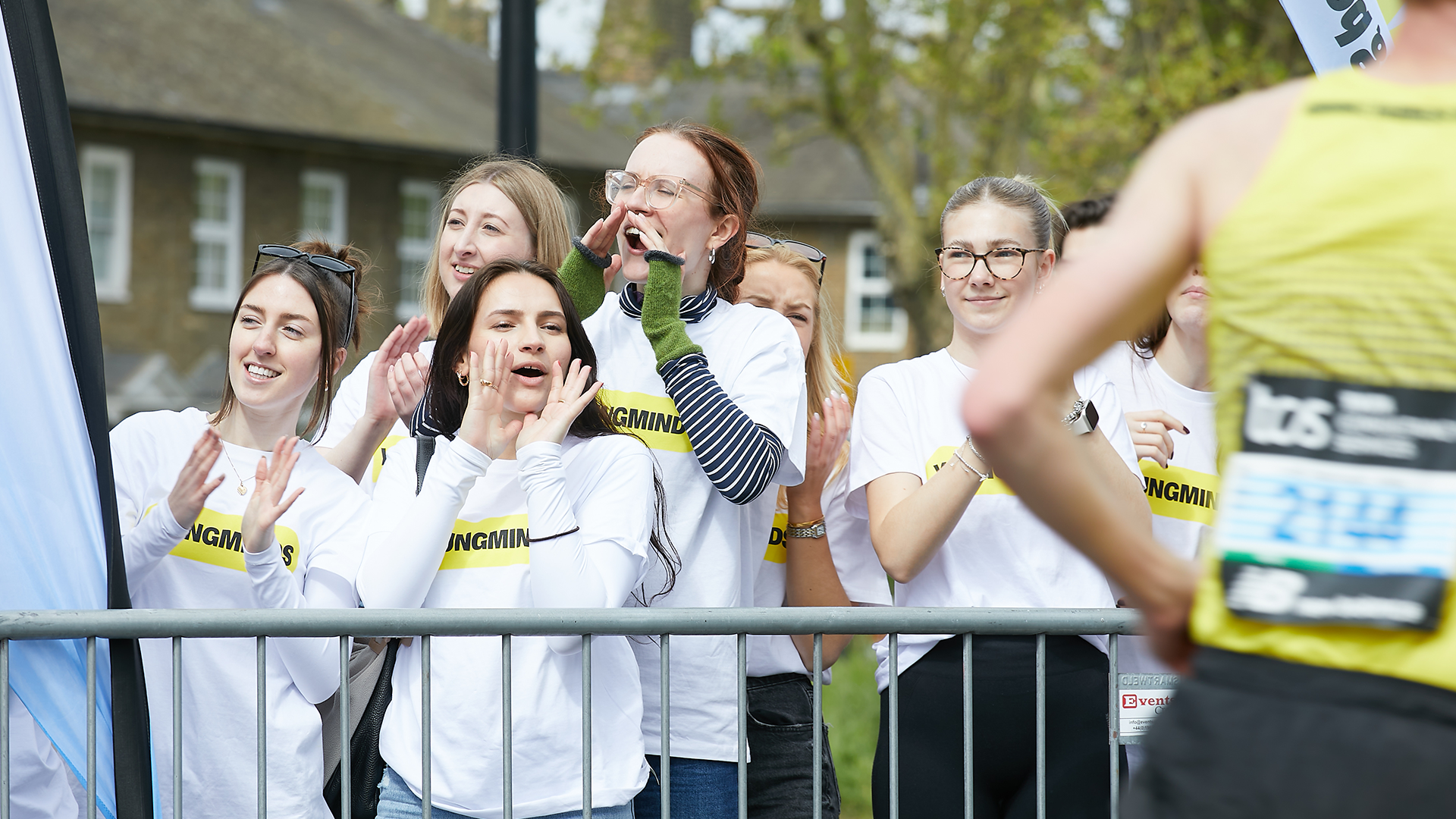 YoungMinds staff cheering marathon runners on from the side line in YoungMinds t-shirts and with YoungMinds banners.