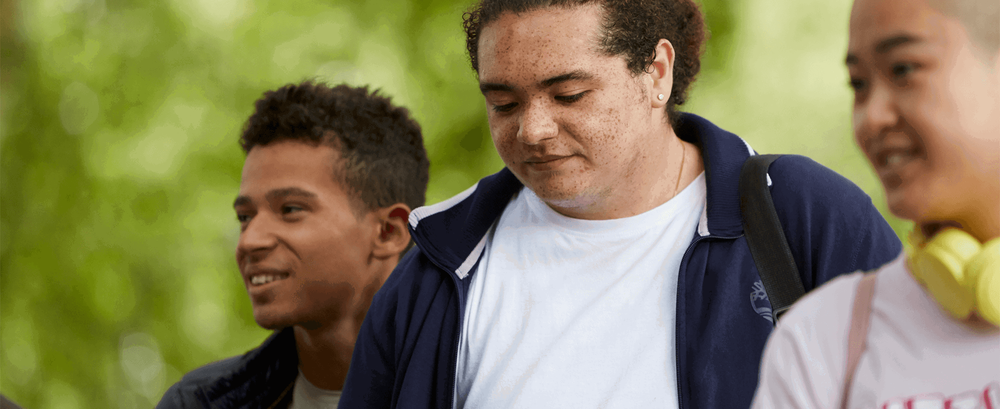 Three young people walk through the woods while talking and smiling together.